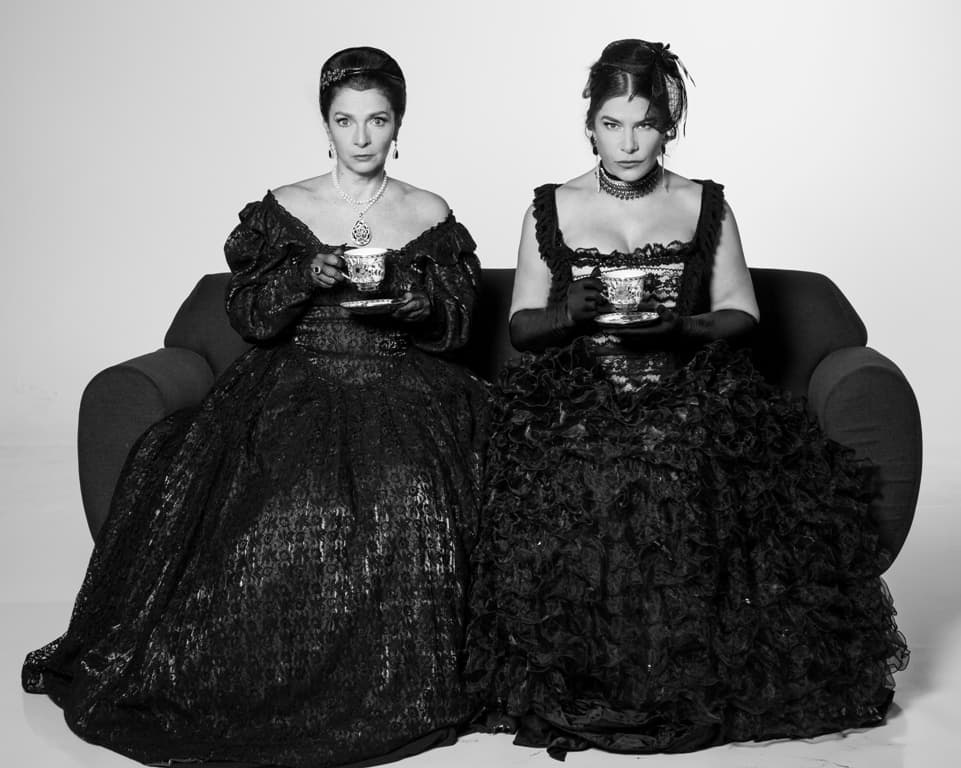 Claudia Ohana e Priscila Fantin sentadas num sofá, com trajes de luto vitoriano, segurando xícaras de chá, em As Amantes de George Washington