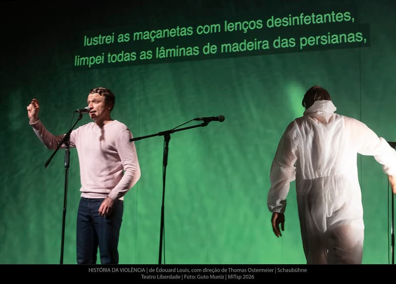 Ator ao microfone com legenda projetada ao fundo: lustrei as maçanetas com lenços desinfetantes