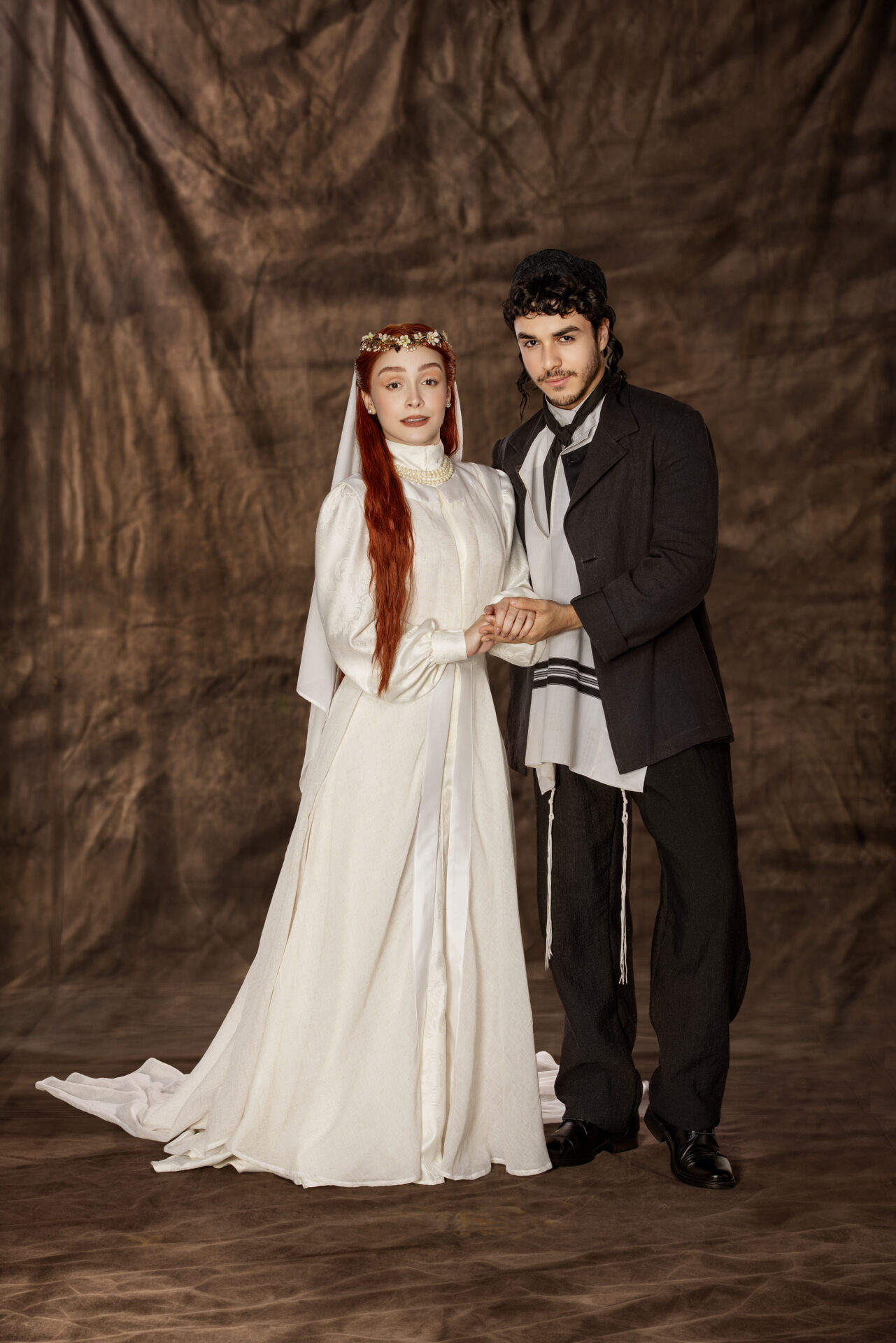 Casal jovem de Dibuk, o Musical, de mãos dadas em figurinos de época