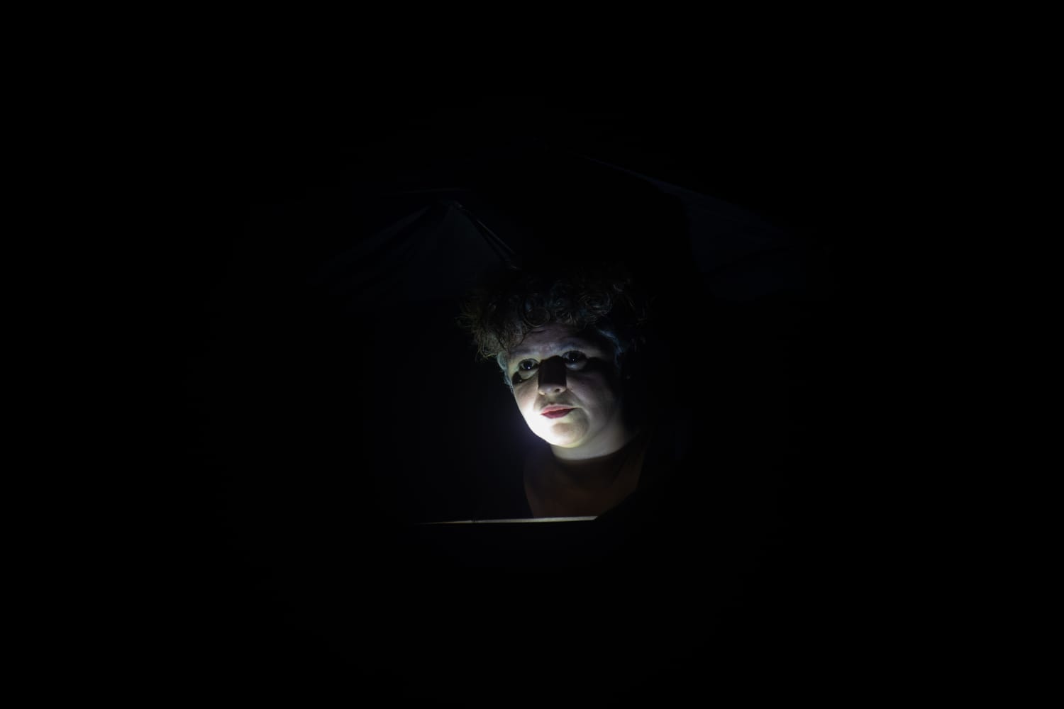 O rosto de Alessandra Queiroz iluminado por baixo, no escuro
