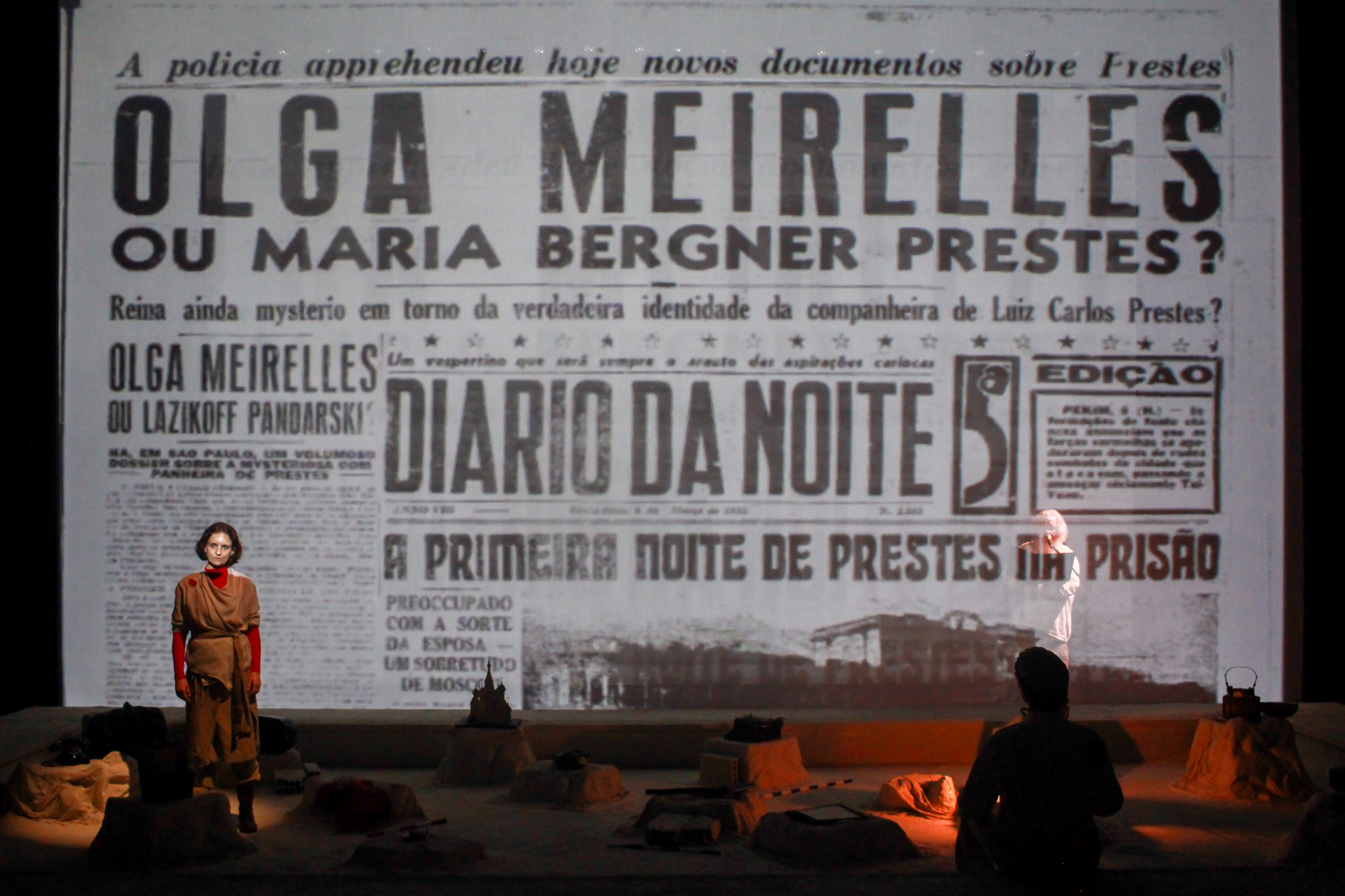Manchete de jornal projetada em cena: Olga Meirelles ou Maria Bergner Prestes?