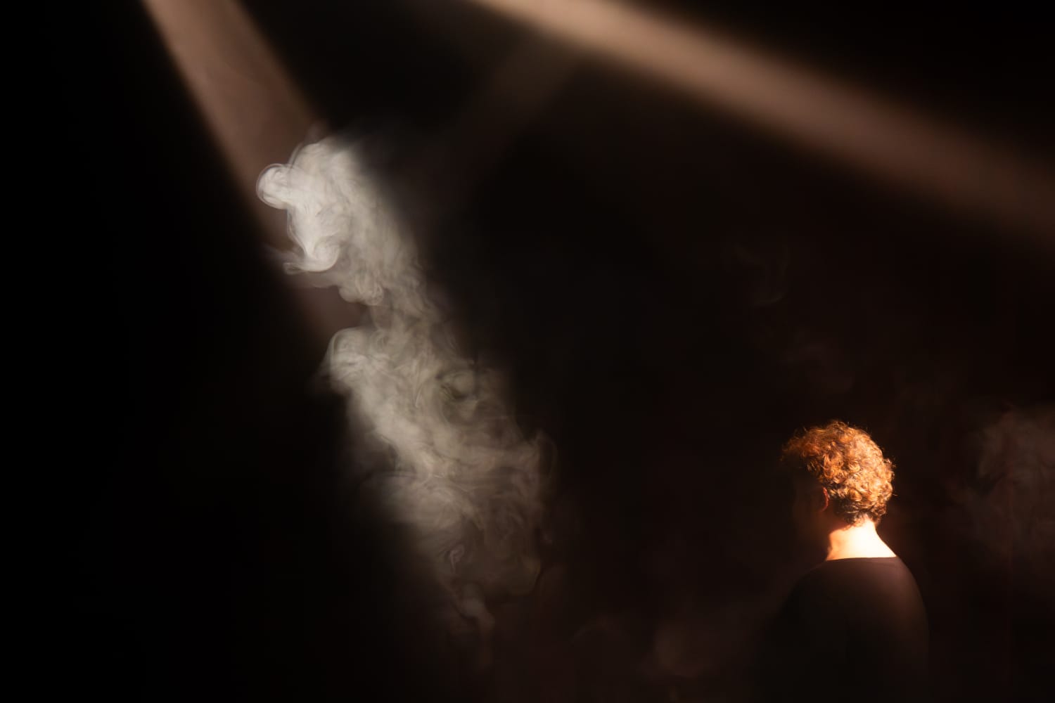 Alessandra Queiroz de costas, no feixe de luz atravessado pela fumaça