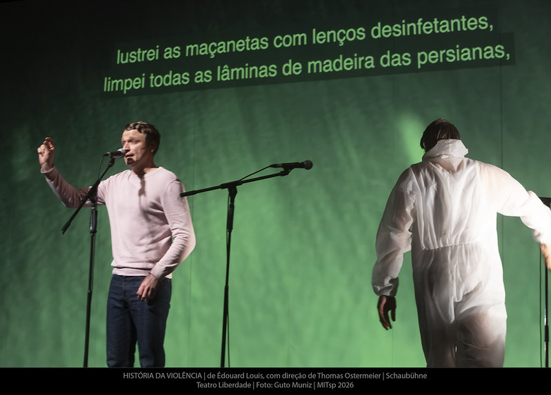 Ator ao microfone com legenda projetada ao fundo: lustrei as maçanetas com lenços desinfetantes