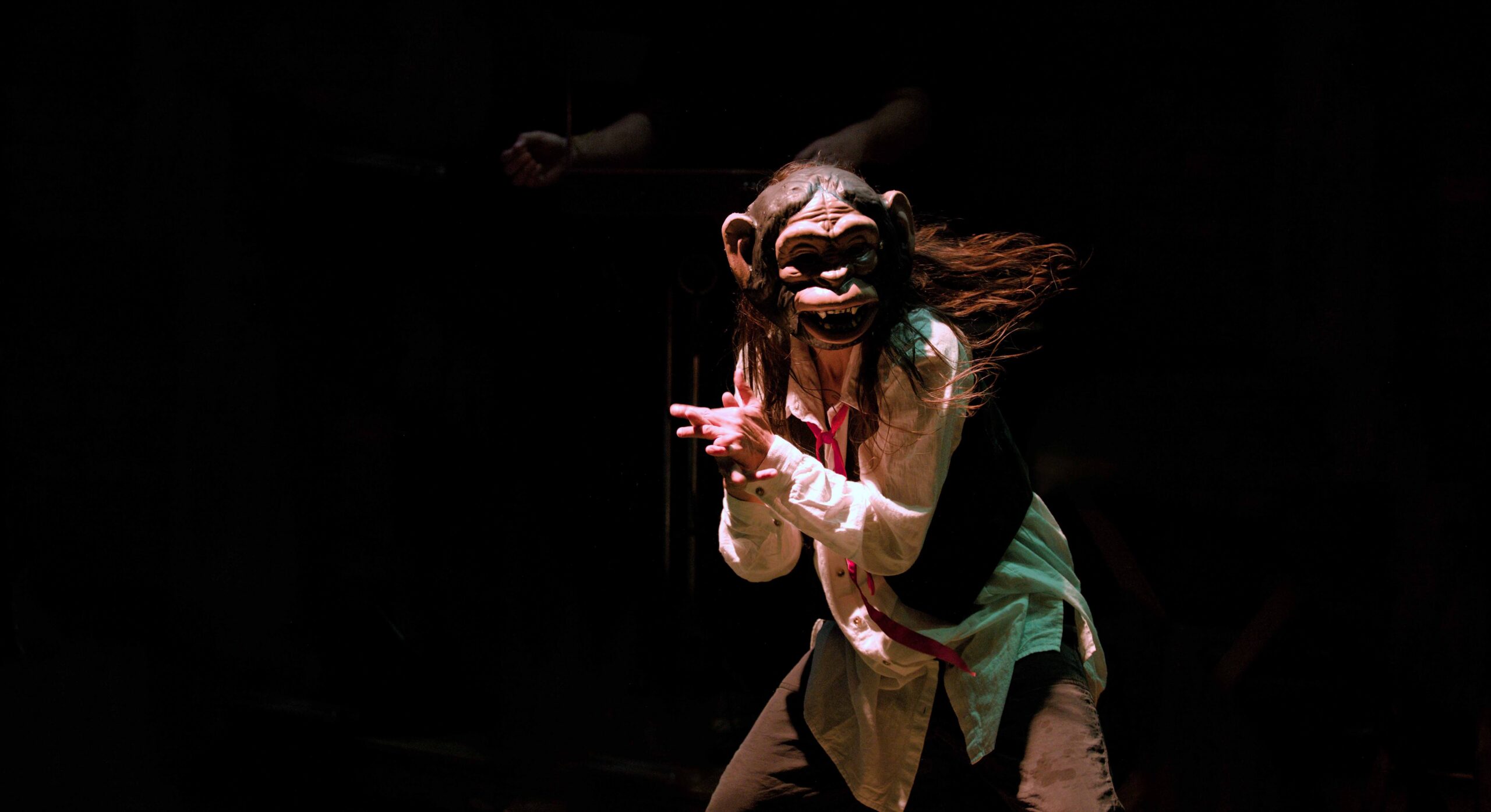 Performer com máscara em cena, com expressividade corporal.