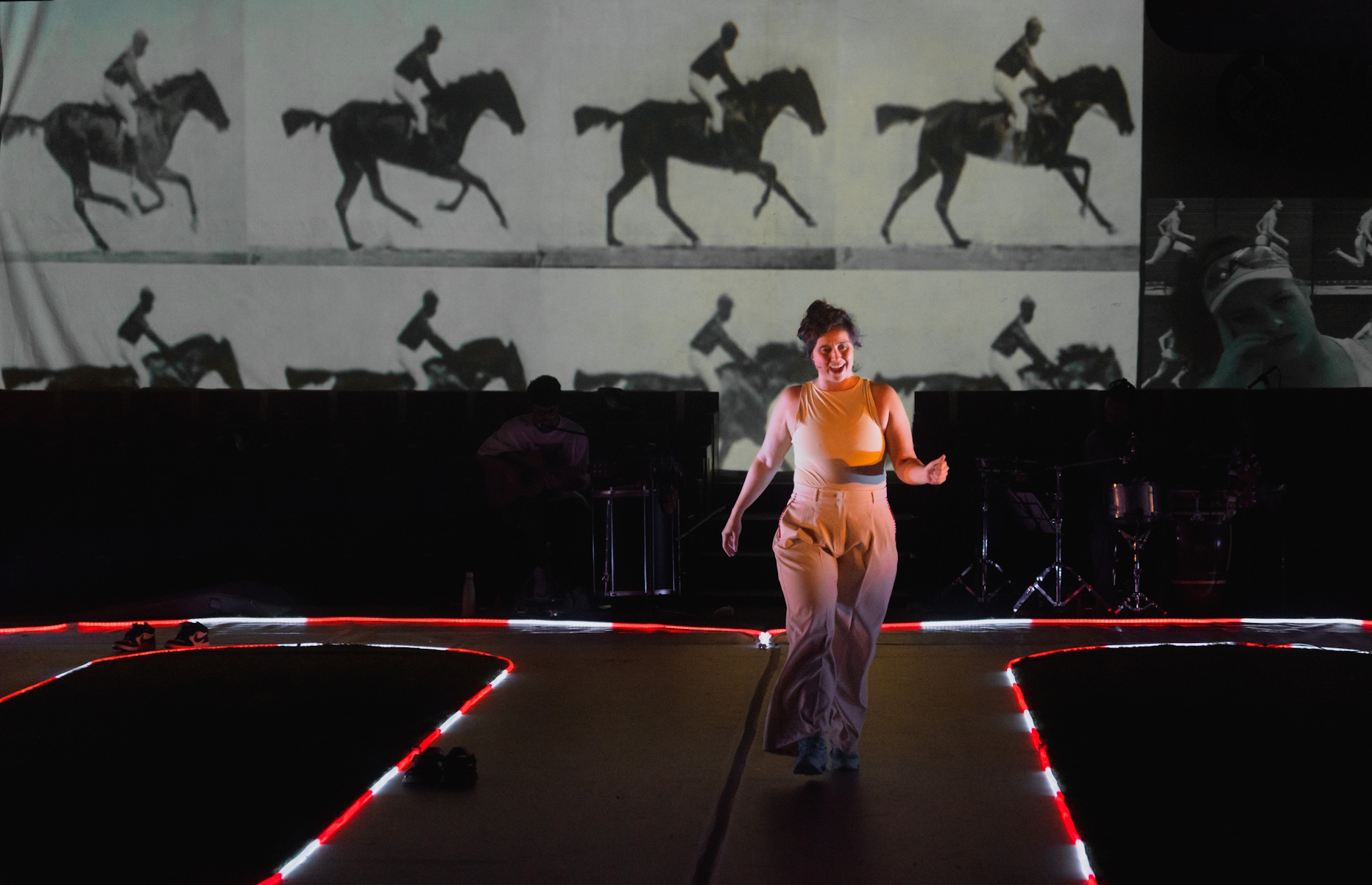 Cena de Pés-Coração com projeção ao fundo e intérprete diante de um carrinho em cena.